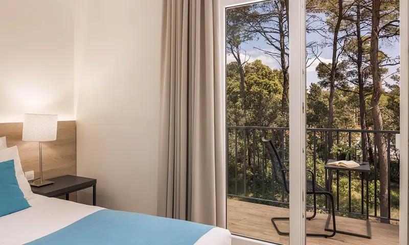 Une chambre lumineuse s'ouvre sur un balcon avec vue sur la végétation.