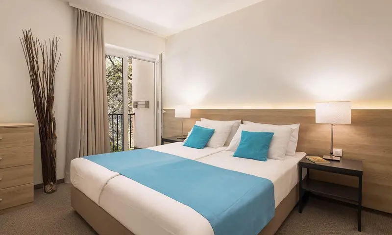 Une chambre lumineuse avec un grand lit recouvert d'une couverture turquoise.