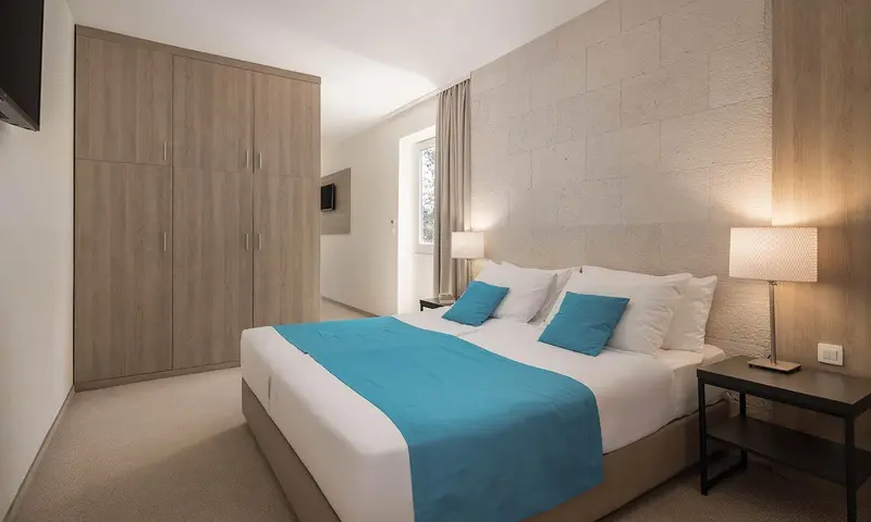 Une chambre lumineuse avec un grand lit recouvert d'une couverture turquoise.