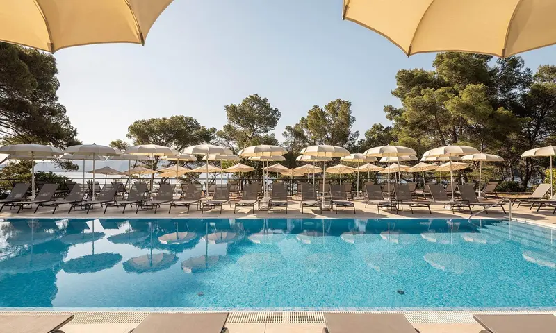 Transats alignés au bord d'une piscine turquoise sous des parasols beiges.