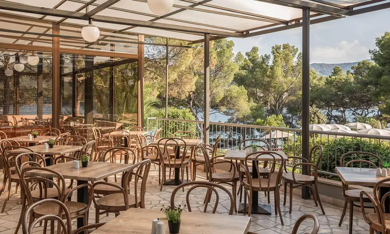 Terrasse ombragée avec tables et chaises donnant sur un paysage côtier.