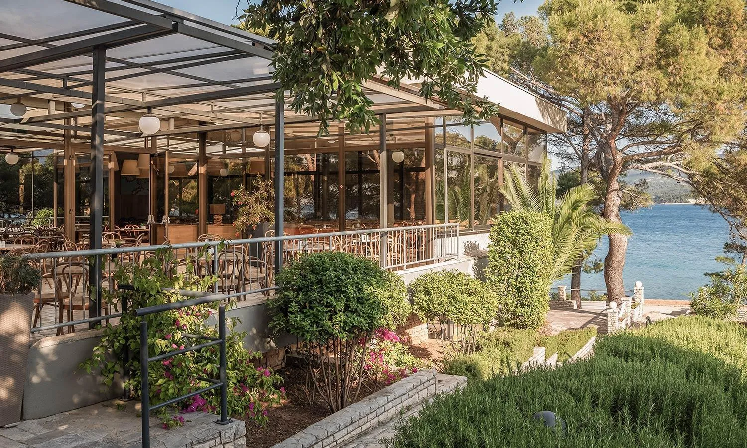 Terrasse ombragée avec tables et chaises donnant sur la mer.