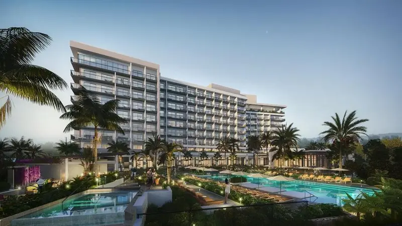 Bâtiment moderne avec des palmiers et des piscines éclairées au crépuscule.