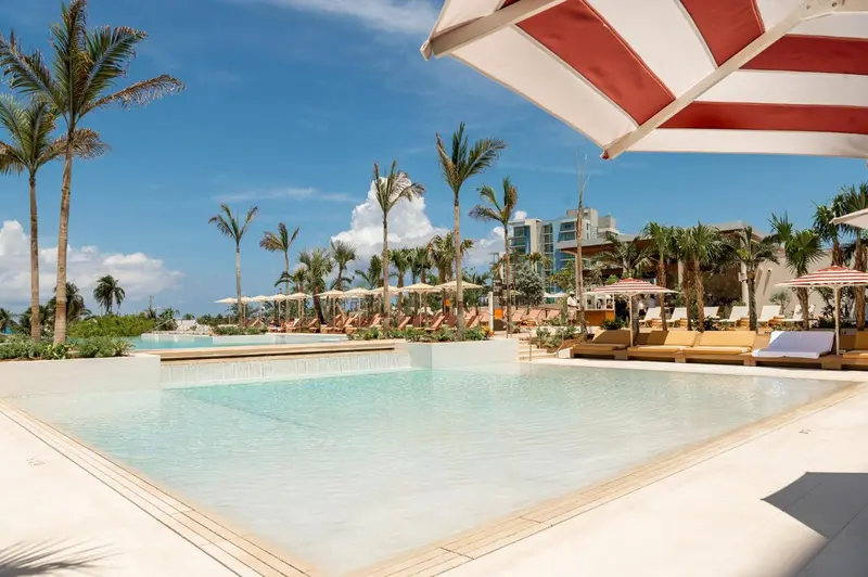 Piscine rectangulaire bordée de transats sous des parasols rayés, avec végétation tropicale en arrière-plan.