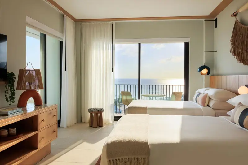 Chambre lumineuse avec deux lits et vue sur la mer.