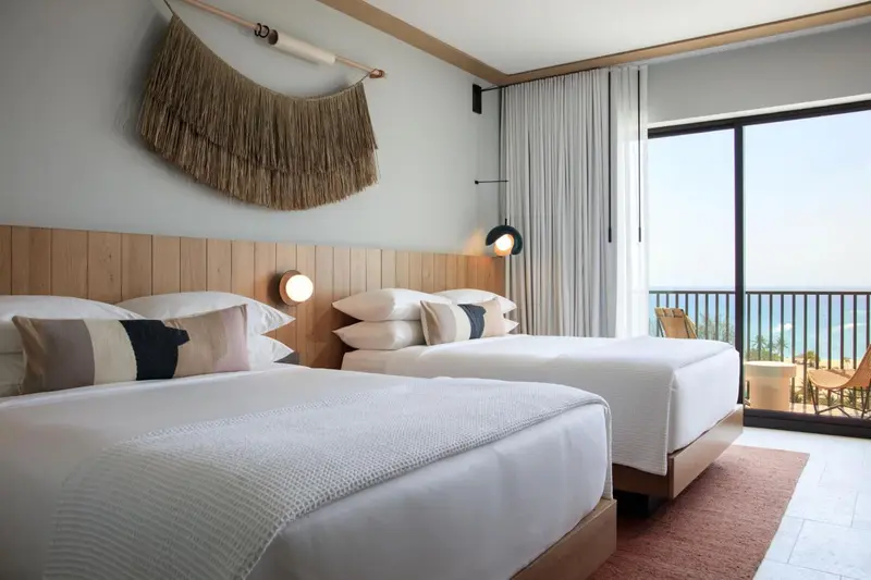 Chambre lumineuse avec deux lits et vue sur la mer.