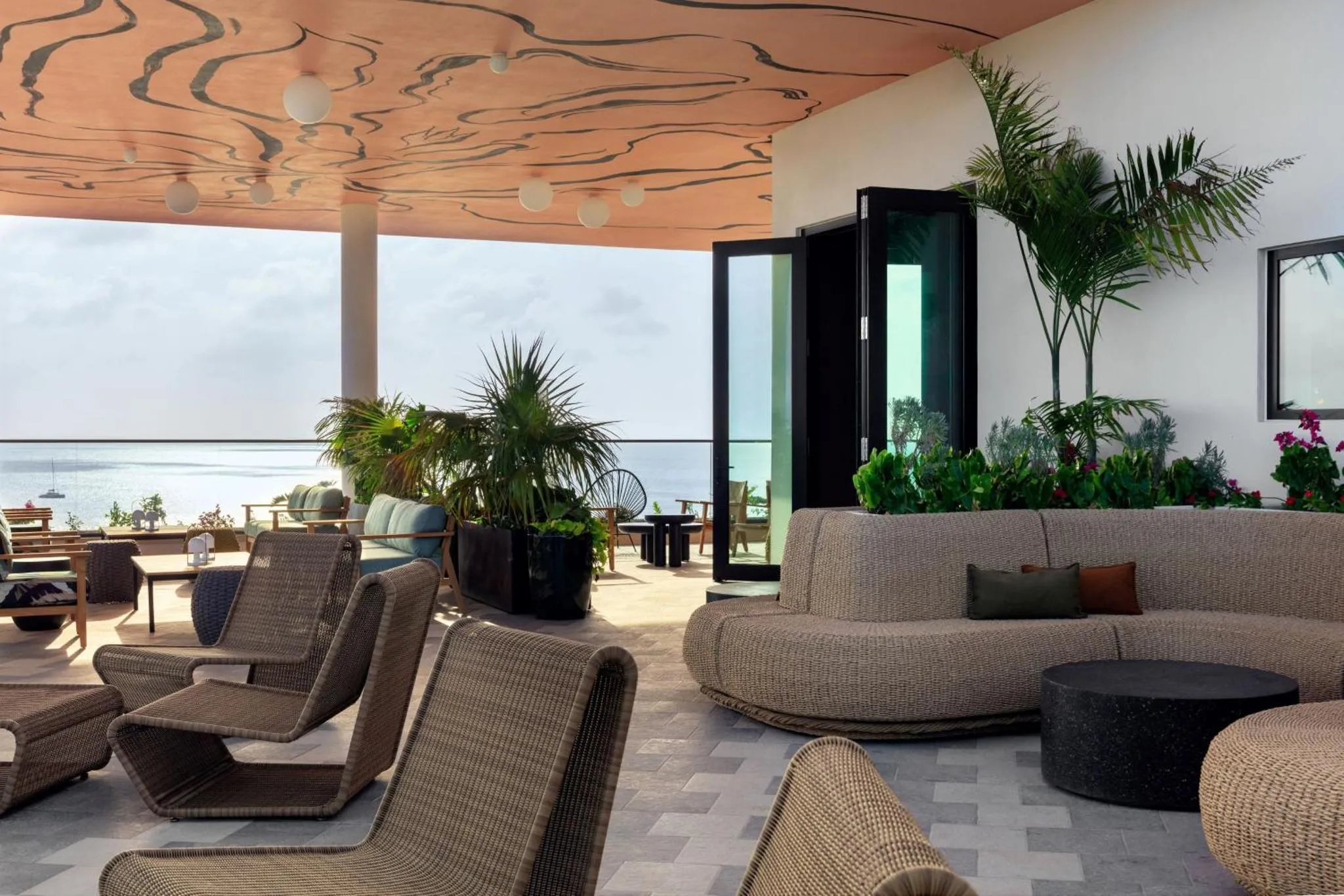 Espace de détente extérieur avec mobilier confortable et végétation tropicale face à la mer.