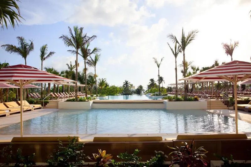 Une piscine rectangulaire bordée de transats sous des parasols rayés rouges et blancs, entourée de végétation tropicale.