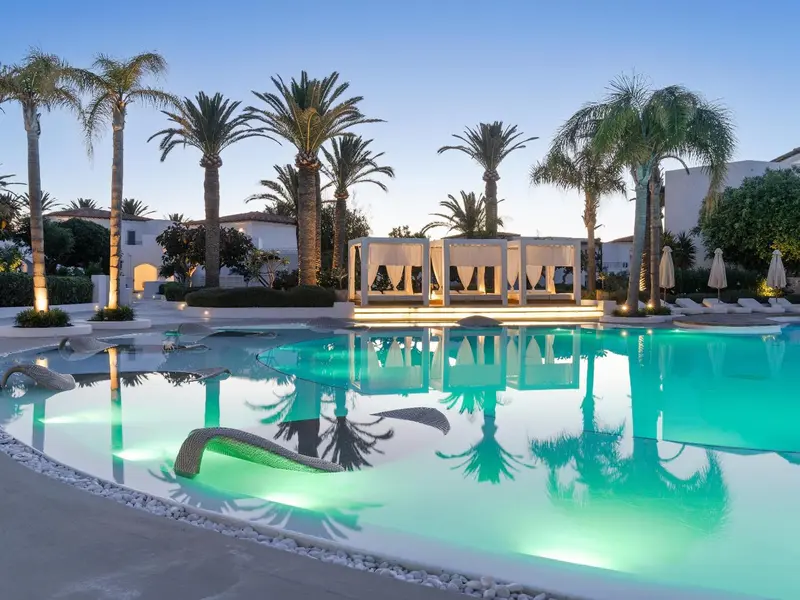 Piscine illuminée avec des palmiers et des transats blancs au crépuscule.