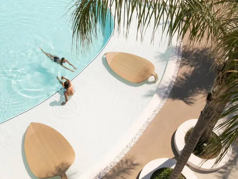 Vue aérienne d'une piscine avec des nageurs et des chaises longues en bois.