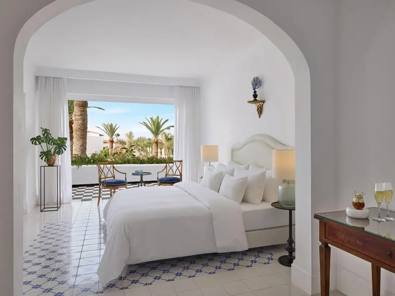 Chambre lumineuse avec un lit blanc et une vue sur une végétation luxuriante.