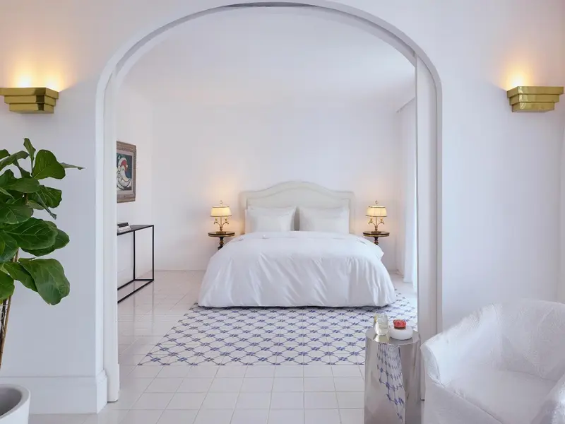 Une chambre lumineuse avec un grand lit blanc et une décoration sobre.
