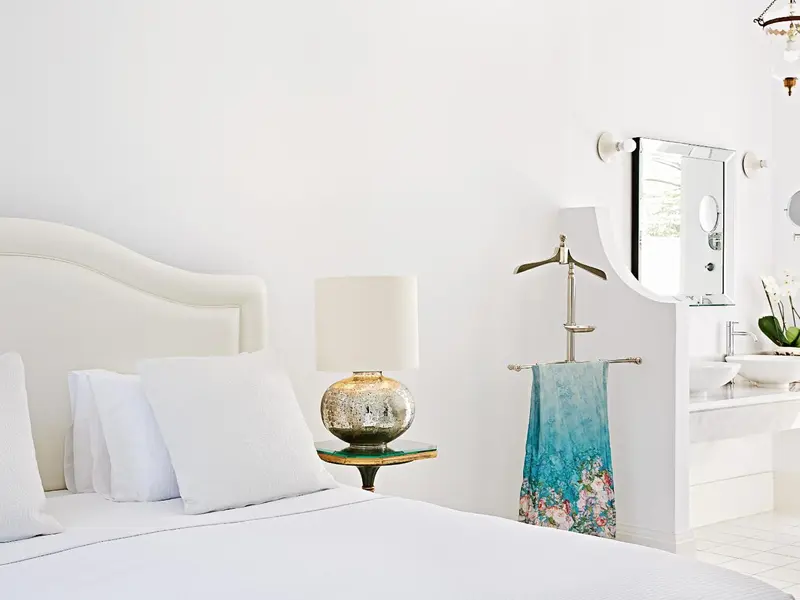 Une chambre lumineuse avec un grand lit blanc et une salle de bain attenante.