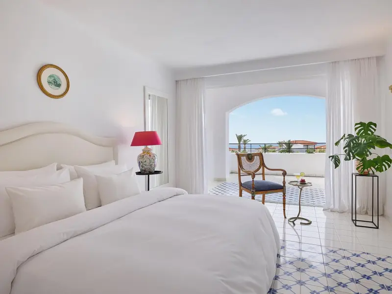 Une chambre lumineuse avec un lit blanc et une vue sur une terrasse ensoleillée.