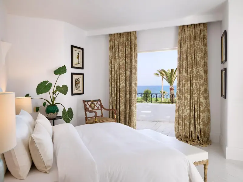 Une chambre lumineuse s'ouvre sur une vue de mer et de végétation.