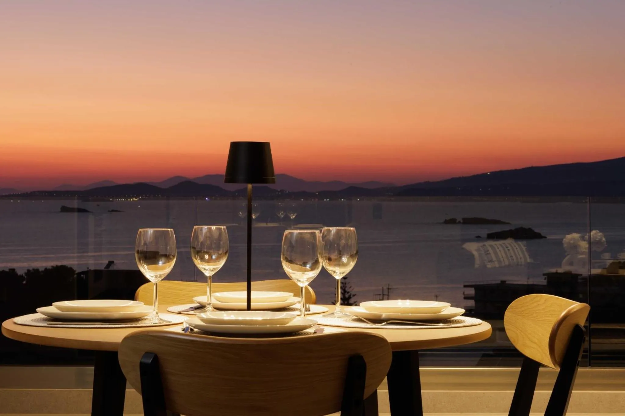 Table dressée avec des verres de vin et des assiettes face à un coucher de soleil sur la mer.