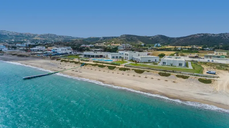 Vue aérienne d'un complexe hôtelier blanc bordant une plage de sable fin et une mer turquoise.