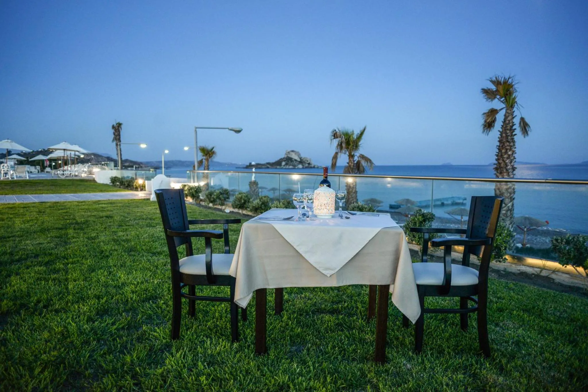 Table dressée pour un dîner en extérieur avec vue sur la mer au coucher du soleil.