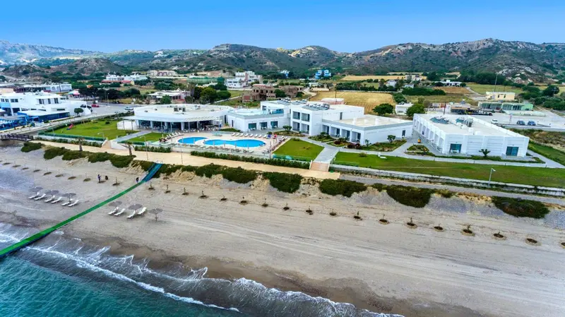 Vue aérienne d'un complexe hôtelier blanc avec piscine et plage.
