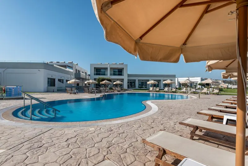 Une piscine rectangulaire bordée de transats sous des parasols beiges.