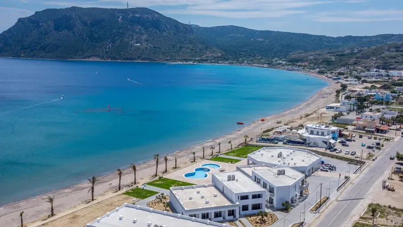Vue aérienne d'une plage de sable blanc bordée de bâtiments blancs et d'une mer turquoise.