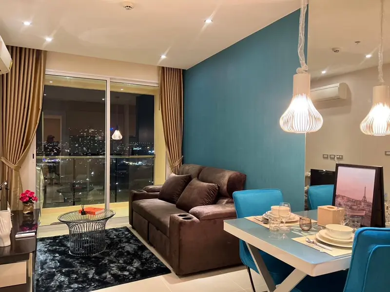 Un salon moderne avec canapé marron et table basse en verre, donnant sur une vue nocturne de la ville.