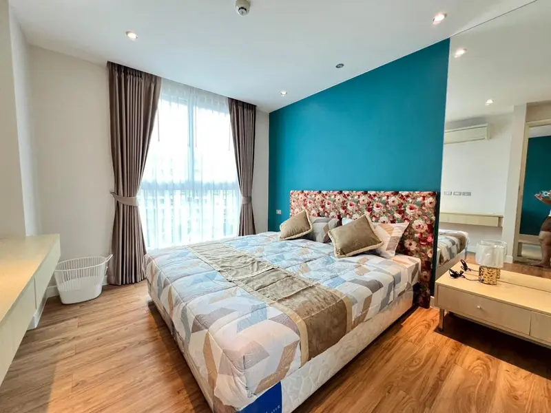 Une chambre lumineuse avec un grand lit et un mur bleu turquoise.