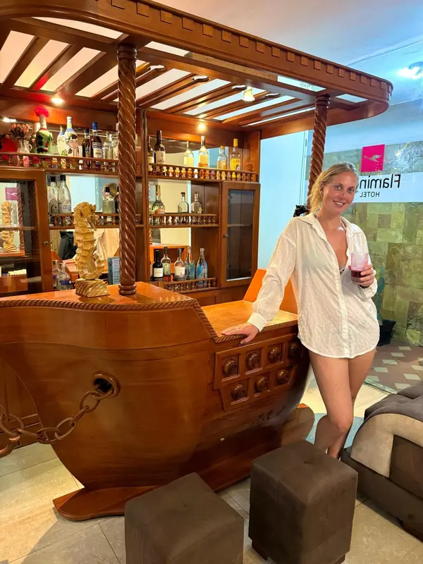 Une femme se tient près d'un comptoir de bar en bois sculpté rempli de bouteilles.