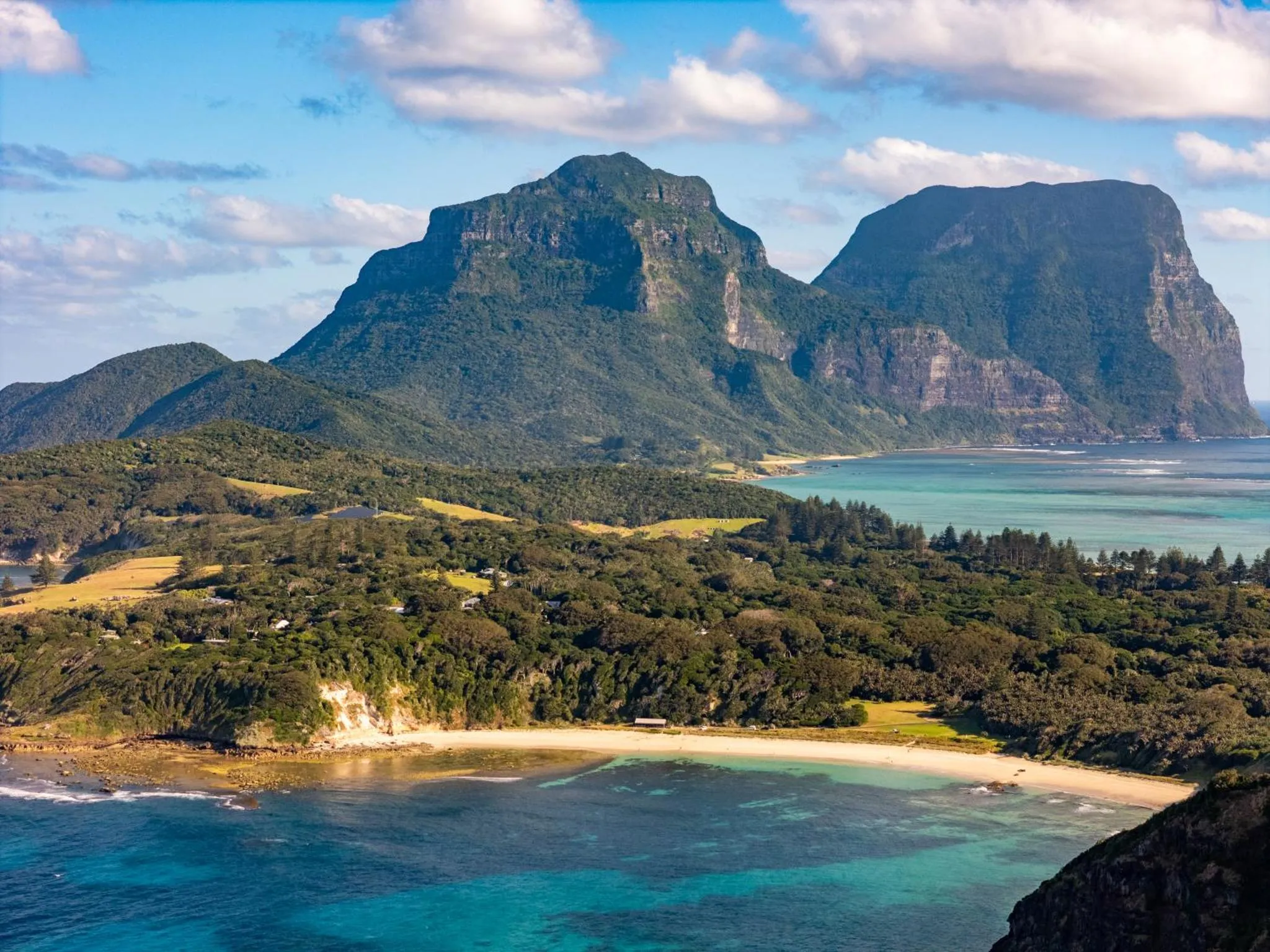 Paysage côtier avec une montagne verdoyante et une plage de sable.