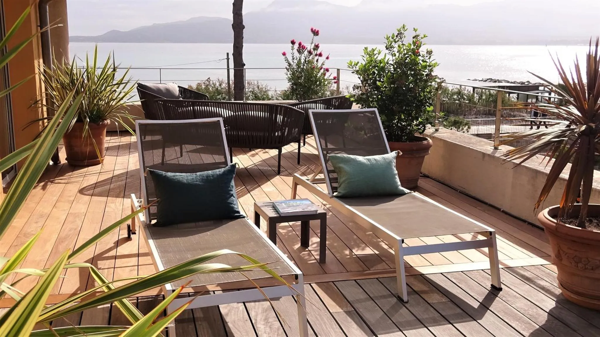 Terrasse aménagée avec des fauteuils et des transats face à la mer.