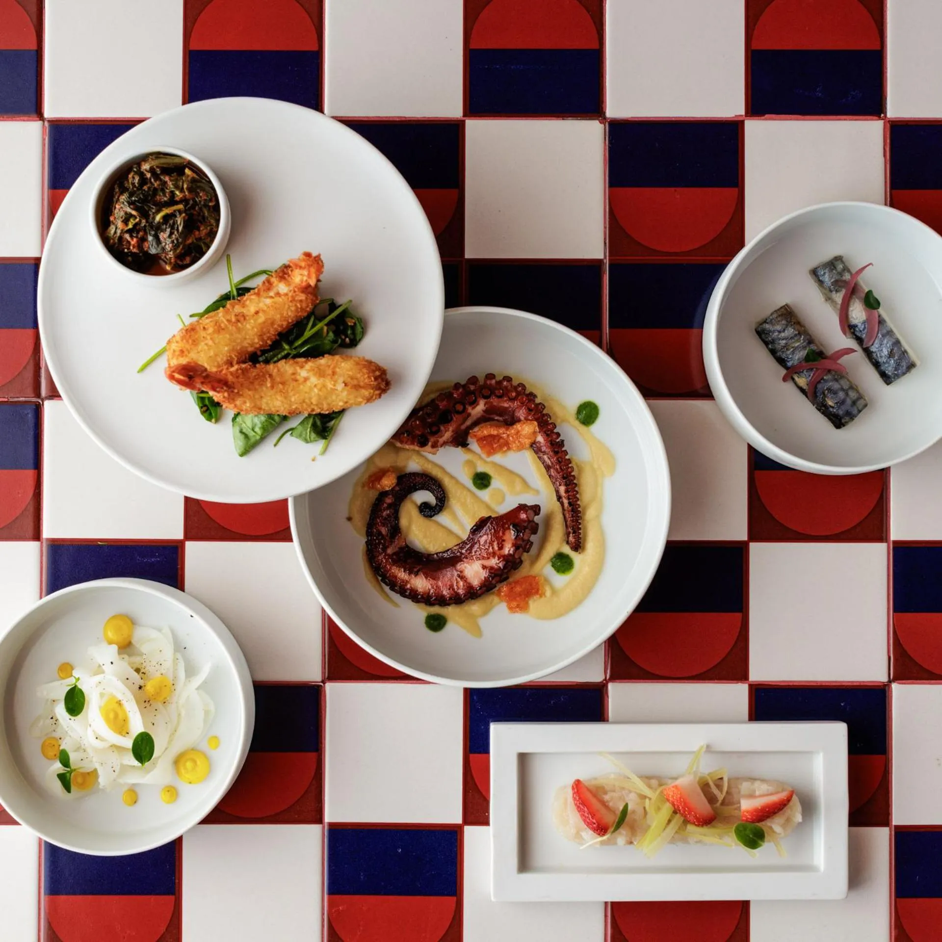 Assiettes de fruits de mer et de légumes disposées sur une table à carreaux colorés.