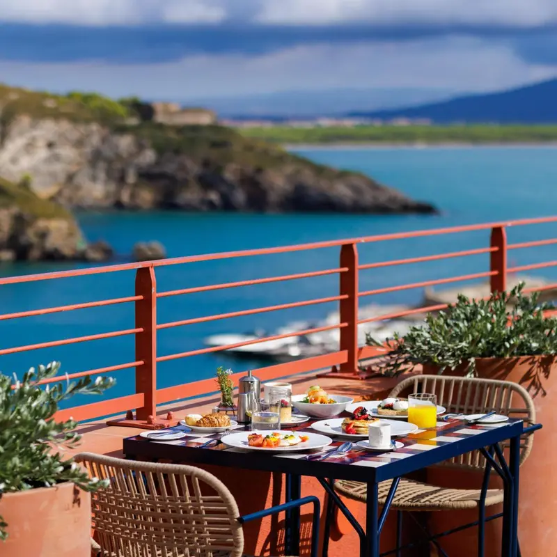 Une table est dressée pour le petit-déjeuner sur une terrasse ensoleillée avec vue sur la mer.
