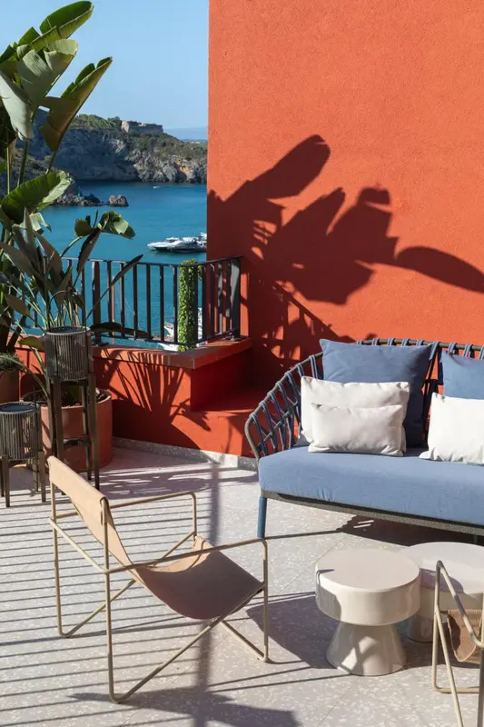 Canapé bleu et fauteuil sur une terrasse ensoleillée avec vue sur la mer.