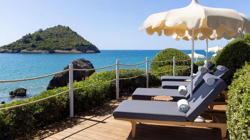 Transats et parasols sur une terrasse surplombant la mer et une île.