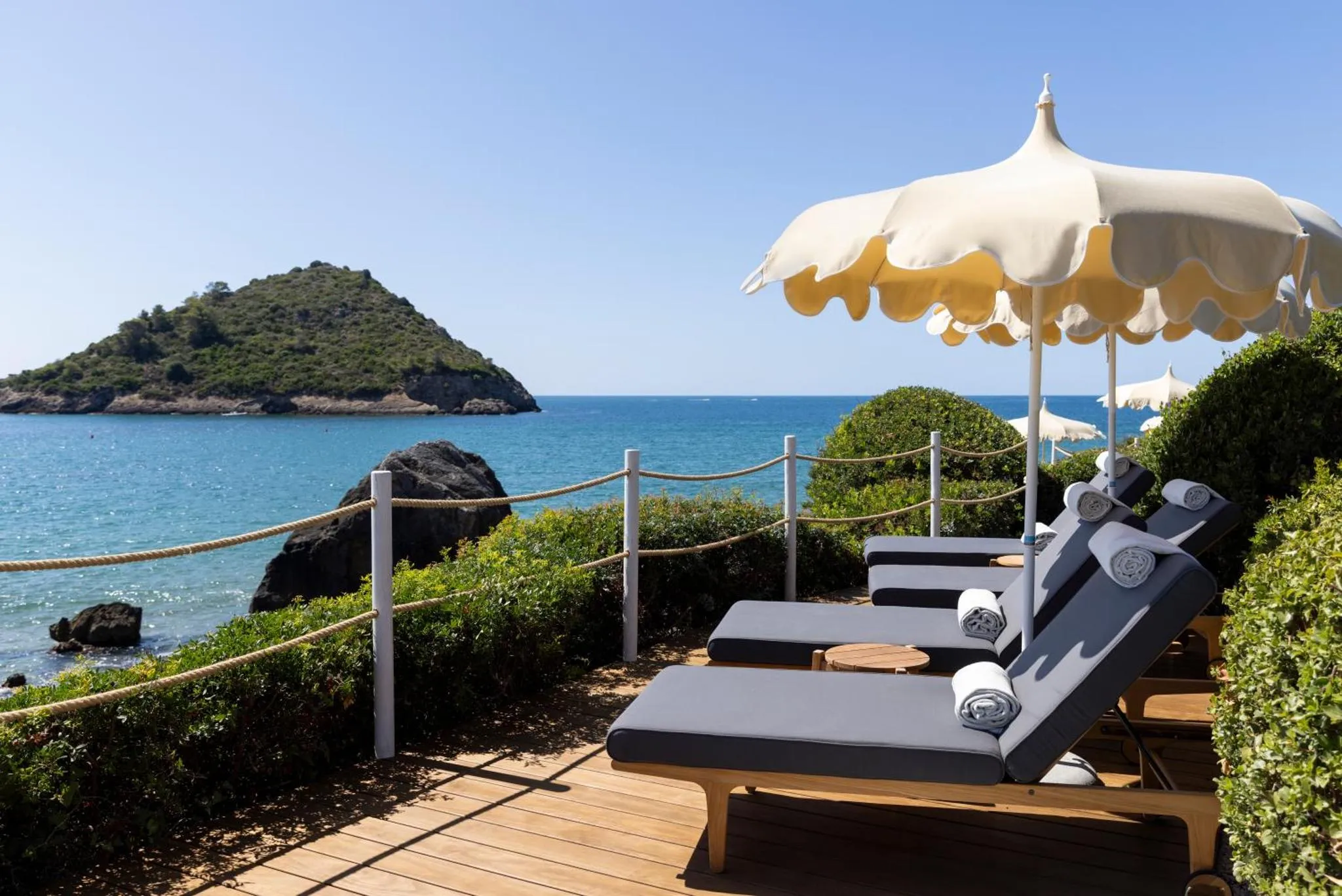 Transats et parasols sur une terrasse surplombant la mer et une île.