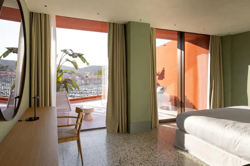 Une chambre lumineuse avec un grand balcon donnant sur un paysage urbain.