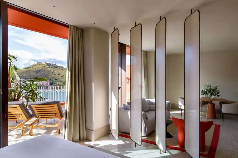 Une chambre lumineuse s'ouvre sur une terrasse avec vue sur la mer et les collines.