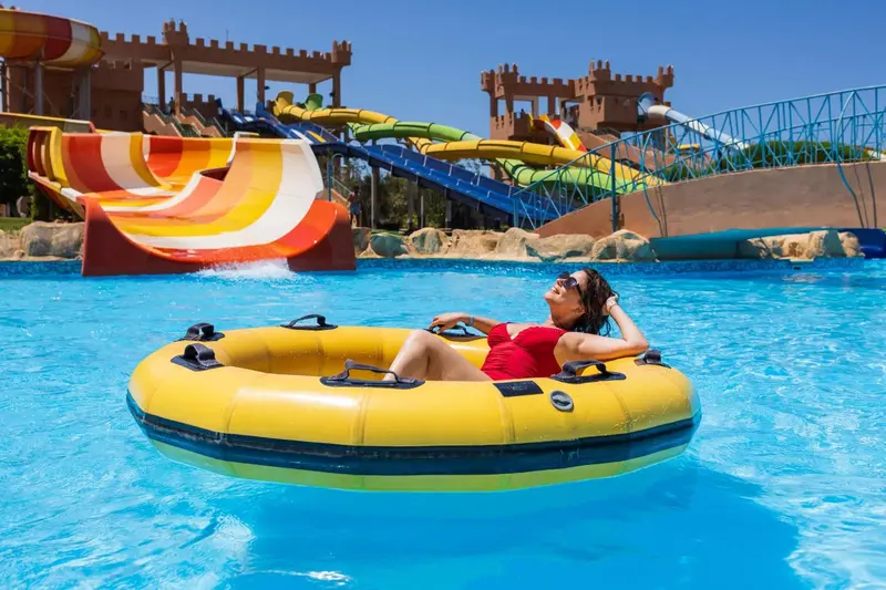 Une femme se détend sur une bouée dans une piscine avec des toboggans colorés en arrière-plan.