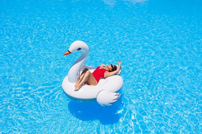 Une femme se détend sur un cygne gonflable dans une piscine ensoleillée.