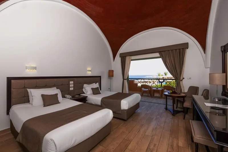 Chambre avec deux lits et vue sur la mer par une fenêtre.