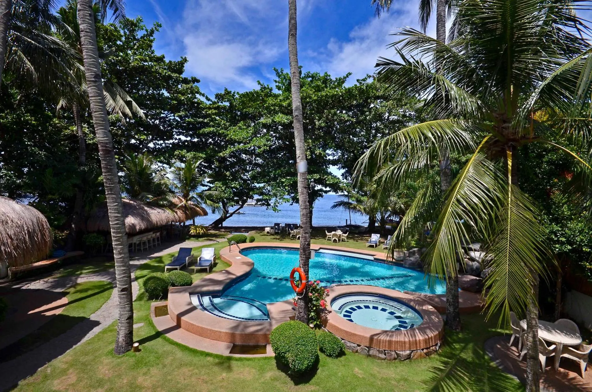 Une piscine bordée de végétation tropicale avec des transats et des parasols.
