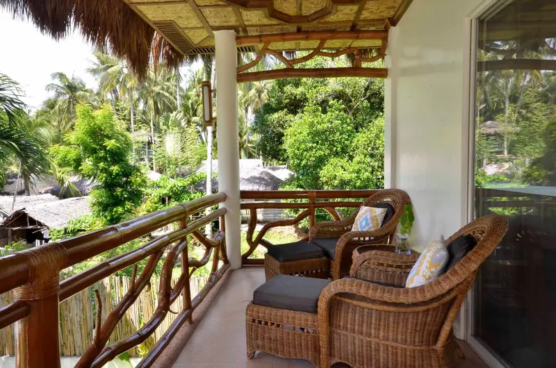 Terrasse ombragée avec mobilier en rotin donnant sur une végétation luxuriante.