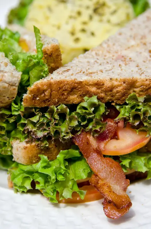 Un sandwich garni de bacon, de laitue, de tomate et de poulet est présenté sur une assiette blanche.