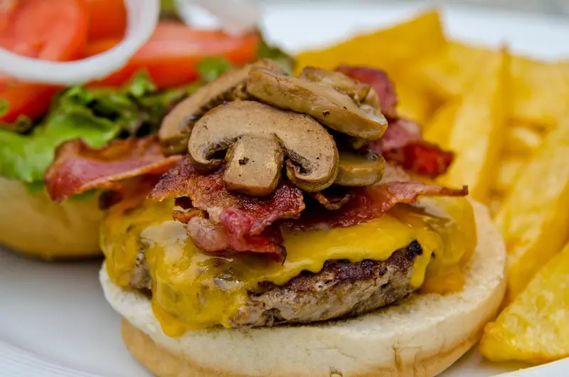 Un hamburger garni de champignons, de bacon et de fromage, accompagné de frites.