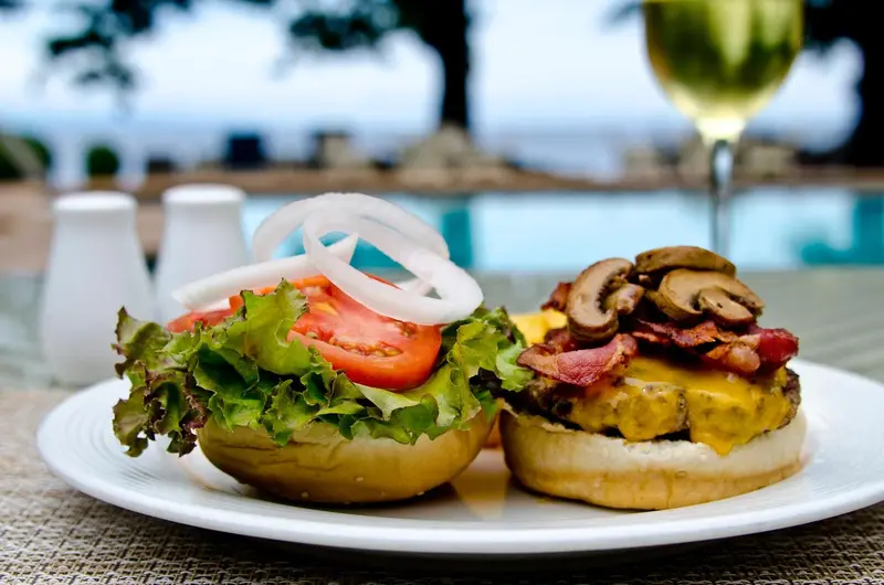 Deux hamburgers garnis sur une assiette blanche, avec une piscine turquoise en arrière-plan.