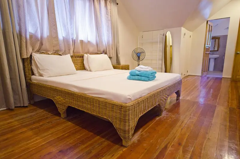 Une chambre lumineuse avec un grand lit en rotin et un parquet en bois.
