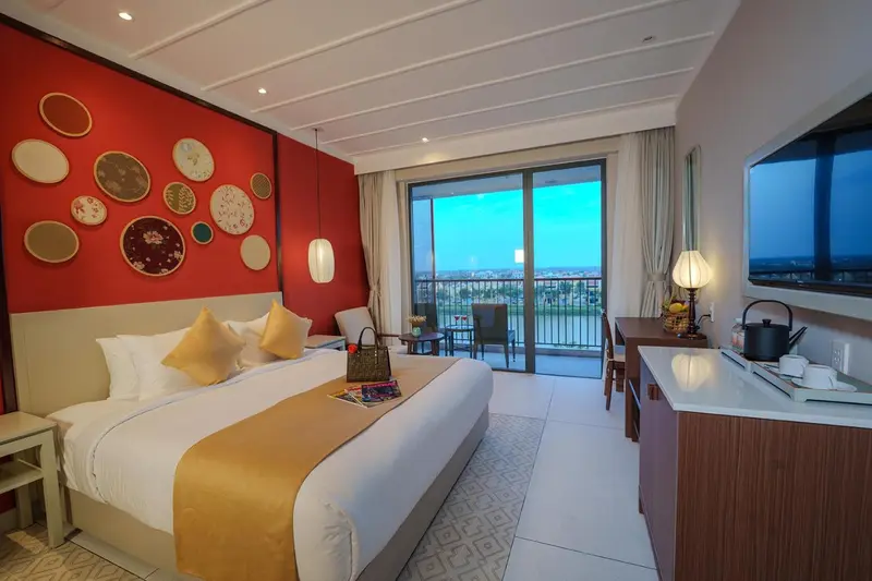 Chambre lumineuse avec un grand lit et une vue sur la mer depuis un balcon.