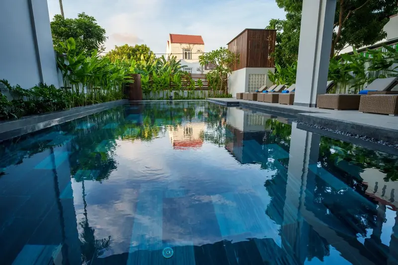 Une piscine rectangulaire turquoise reflète le ciel et la végétation environnante.