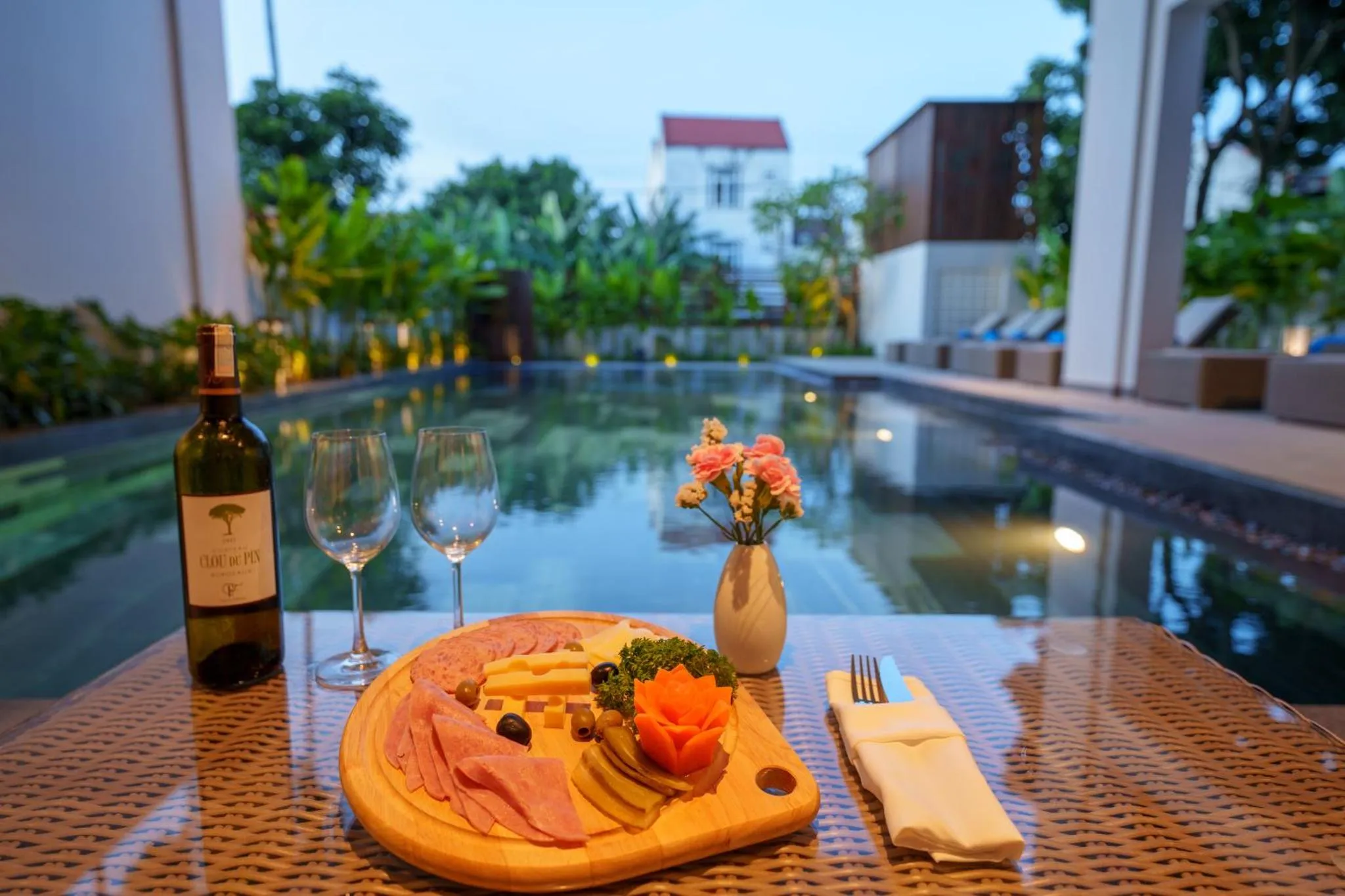 Une table est dressée avec une bouteille de vin, des verres et une assiette de charcuterie près d'une piscine.