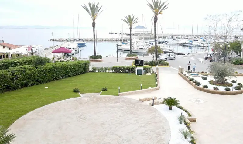 Vue aérienne d'un jardin verdoyant devant un port de plaisance ensoleillé.